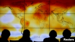 FILE - Participants are seen in silhouette as they look at a screen showing a world map with climate anomalies during the World Climate Change Conference 2015 (COP21) at Le Bourget, near Paris, France, Dec. 8, 2015. 