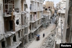 Residents walk near damaged buildings in the Old City of Aleppo, Syria, May 5, 2016.