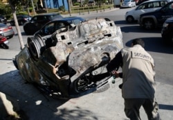 A private security worker photgraphs a car burned by supporters of the Shiite Hezbollah and Amal groups in Beirut, Dec. 17, 2019. The groups were angered by a video that showed a man insulting Shiite figures.