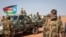 A South Sudanese government soldier stands with others near their vehicles, after government forces on Friday retook from rebel forces the provincial capital of Bentiu, in Unity State, South Sudan, Sunday, Jan 12, 2014.