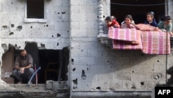 Children play in the balcony of an apartment next to a man checking the destruction after an Israeli strike in the Nuseirat camp, in the central Gaza Strip, Dec. 10, 2024.