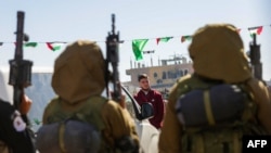 ষষ্ঠ জিম্মি-বন্দী বিনিময়ের অংশ হিসাবে গাজা ভূখন্ডের দক্ষিণাঞ্চল খান ইউনিসে রেড ক্রসের একটি দলের কাছে হস্তান্তর করার আগে হামাস জঙ্গিরা জিম্মি ইসরায়েলি-রাশিয়ান নাগরিক সাশা ট্রুপানভকে নিয়ে যাচ্ছে। ১৫ ফেব্রুয়ারি ২০২৫।