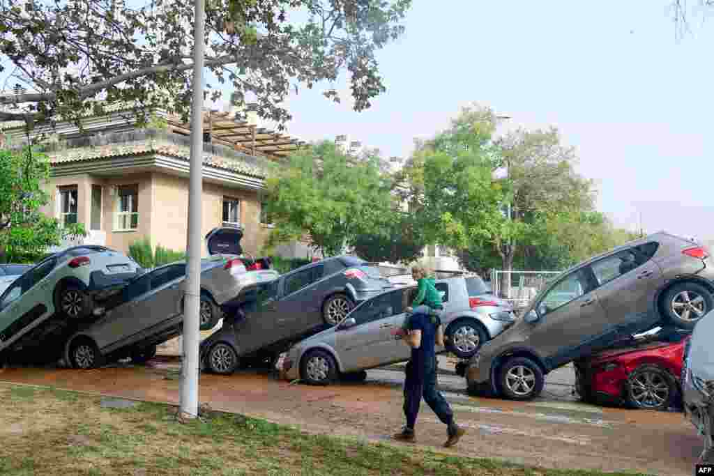 Residents walk past piled up cars following deadly floods in Valencia's De La Torre neighborhood, south of Valencia, eastern Spain. Floods triggered by torrential rains in Spain's eastern Valencia region have left at least 70 people dead.