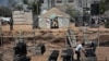 FILE - Two Palestinian boys stand outside a tent, background, watching workers rebuild a house which was destroyed during the 2014 summer war between Israel and Hamas, as the long-awaited reconstruction began in Shijaiyah neighborhood eastern Gaza City, July 23, 2015.