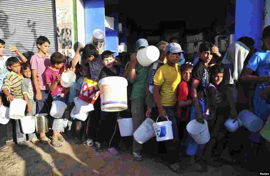Boys carry buckets as they line up to receive free food for their first iftar, or breaking fast, during Ramadan in Raqqa province, eastern Syria July 10, 2013. 