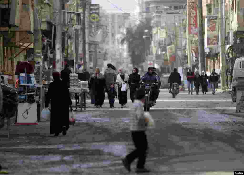 People walk along a street as men ride on a motorcycle in Deir al-Zor, Feb. 4, 2014.