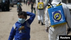FILE - FILE - An internally displaced Syrian girl wears a face mask as members of the Syrian Civil defense sanitize the Bab Al-Nour internally displaced persons camp, to prevent the spread of coronavirus disease (COVID-19) in Azaz, Syria, March 26, 2020.