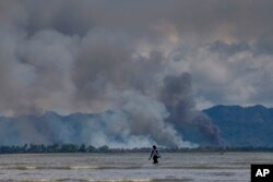 A Bangladeshi boy walks towards a parked boat as smoke rises from across the border in Myanmar, at Shah Porir Dwip, Bangladesh, Sept. 14, 2017.