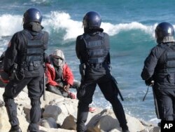 FILE - A migrant faces Italian police officers in riot gear after the evacuation of a tent camp at the Franco-Italian border in Ventimiglia, Italy, Sept. 30, 2015.