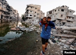Seorang pria Palestina menggendong anak-anaknya saat dia berjalan di samping bangunan yang hancur akibat serangan Israel, di Khan Younis. (Foto: Reuters)