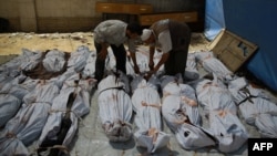 FILE - A Syrian emergency personnel and a civilian inspect the bodies of Syrian men outside a makeshift hospital in a rebel-held area of Douma, east of the capital Damascus, Aug. 12, 2015.