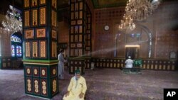 A Kashmiri municipal worker sprays disinfectants as a precautionary measure against coronavirus inside a Muslim shrine as devotees pray in Srinagar, Indian controlled Kashmir, Aug. 16, 2020.