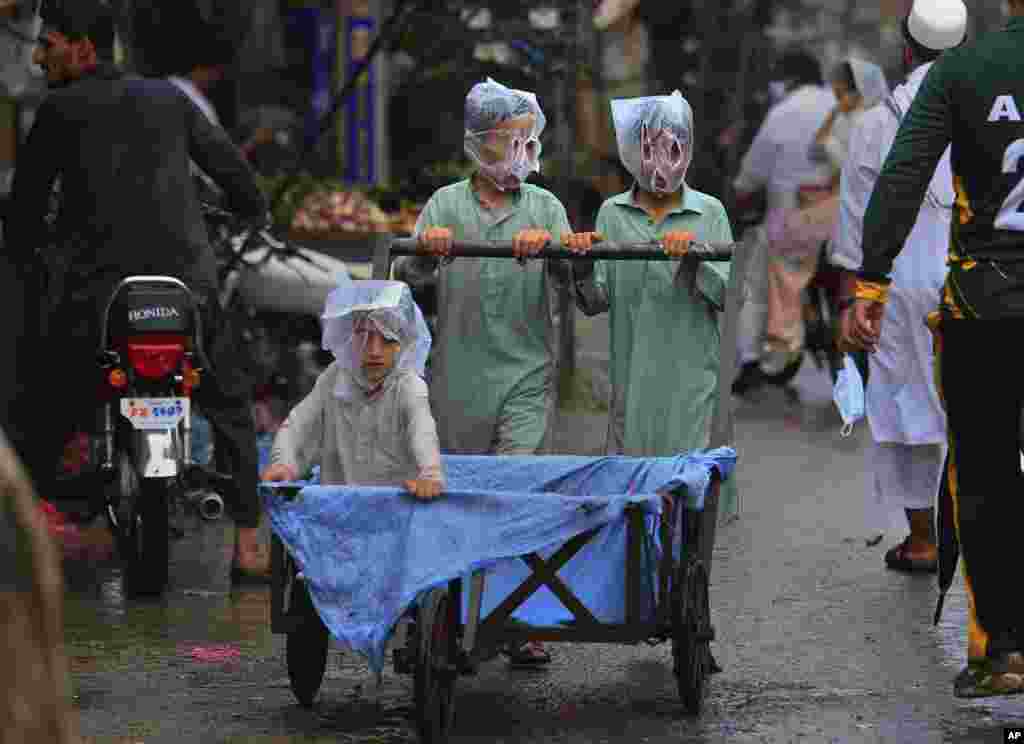 Boys cover their faces with plastic bags while pushing a handcart during rainfall in Peshawar, Pakistan.