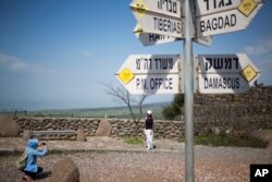 Tourists pose for photograph next to a mock road sign for Damascus, the capital of Syria, and other capitals and cities, in an old outpost in the Golan Heights near the border with Syria, March 22, 2019.