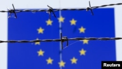 Barbed wire is seen in front of a European Union flag at an immigration reception center in Bicske, Hungary, June 25, 2015. 