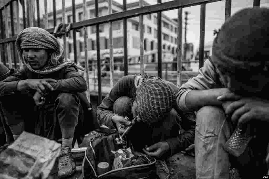 A man smoking methamphetamine on the bridge in the Pul-e-Sukhta area in Kabul sitting with other drug users. (Maciej Stanik/VOA)