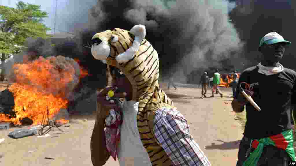 Les manifestants se tiennent devant le parlement où des voitures et des documents brulent, à Ouagadougou le 30 Octobre, 2014. Des centaines de manifestants en colère au Burkina Faso ont pris d&#39;assaut le parlement le 30 Octobre avant d&#39;y mettre le feu en signe de protestation contre l&#39;intention de modifier la Constitution pour permettre au Président Blaise Compaoré pour étendre son règne de 27 ans. AFP PHOTO / ISSOUF SANOGO 