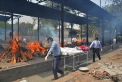 FILE - Relatives carry the body of a person who died of COVID-19 as multiple pyres of other COVID-19 victims burn at a crematorium in New Delhi, India.