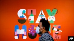 A man wearing a face mask walks in front of a poster recommending people to stay at home, at a department store in Berlin, Germany, April 20, 2020. 