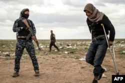 A man suspected of being an Islamic State (IS) group's fighter walks by a member of the Kurdish-led Syrian Democratic Forces (SDF) as he waits to be searched after leaving the IS group's last holdout of Baghouz, Syria, Feb. 27, 2019.