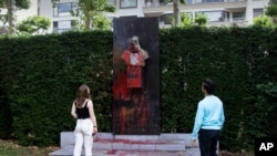 A couple stop to look at a bust of Belgium's King Leopold II, which has been damaged by red paint, graffiti and cement, at a park in Ghent, Belgium, June 19, 2020.