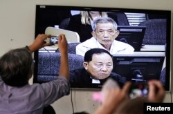FILE - Journalists take photographs of a television screen showing the trial of Kaing Guek Eav, alias Duch, former chief of the S-21 prison, at the Extraordinary Chambers in the Courts of Cambodia (ECCC) on the outskirts of Phnom Penh, Feb. 3, 2012.