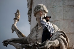 FILE - A demonstrator clenches her fist as she stands on a statue on the Place de la Republique during a rally against racism in Paris, June 9, 2020.