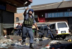 A riot police officer throws a tear gas canister as looters make off with goods from a store in Germiston, east of Johannesburg, South Africa, Sept. 3, 2019.