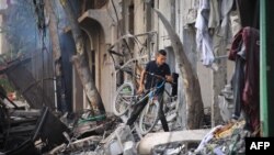 গাজার নুসেইরাত শিবিরে ইসরায়েলি হামলার পর এক ফিলিস্তিনি কিশোর তার সাইকেল নিয়ে ধ্বংসস্তূপ পার হচ্ছে। ফটোঃ ৯ জুন, ২০২৪। 