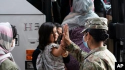 FILE - In this Aug. 30, 2021, photo, Army Pfc. Kimberly Hernandez gives a high-five to a girl evacuated from Kabul, before boarding a bus after they arrived at Washington Dulles International Airport.