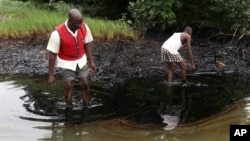 FILE - Men walk in an oil slick covering a creek near Bodo City in the oil-rich Niger Delta region of Nigeria, June 10, 2010.