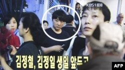 Một thanh niên Nam Triều Tiên đang xem tin trên TV, tại một trạm xe lửa, nói về Kim Jong Chol dự buổi trình diễn của Eric Clapton ở Singapore