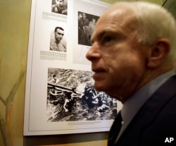 FILE - U.S. Sen. John McCain, R-Ariz, is seen during a tour of Hoa Lo Prison site, Hanoi, April 8, 2009. The photo behind McCain is that the Hanoi army and people pull out McCain out of Truc Back Lake on Oct. 26, 1967 after his plane was shot down.