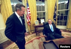 FILE - U.S. President George W. Bush sits at his desk in the Oval Office for the first time on Inaugural Day, in this January 20, 2001 file photo, as his father, former President George H.W. Bush looks on.