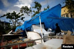 FILE - Joe Quirindongo tries to repair a makeshift tent where he keeps some belongings at the squatter community of Villa Hugo in Canovanas, Puerto Rico, Dec. 9, 2017.