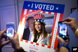 FILE - A woman wearing a US patriotic top hat poses for a photograph in the foreground of a cardboard figure depicting Donald Trump Republican presidential candidate during the Election Night Party at the US Embassy in Budapest, Hungary, Nov. 8, 2016.