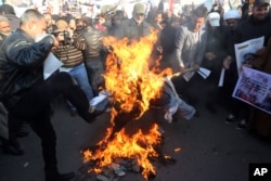 Followers of Shi'ite cleric Muqtada al-Sadr burn an effigy of King Salman of Saudi Arabia as they hold posters of Sheik Nimr al-Nimr during a demonstration in Baghdad, Iraq, Jan. 4, 2016.