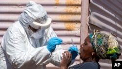 FILE - A woman opens her mouth so that a health worker can collect a sample for coronavirus testing at Lenasia South, south Johannesburg, South Africa, April 21, 2020.