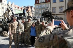 FILE - A woman takes a picture with U.S. soldiers, who are part of a NATO multinational battalion on their way from Germany to Orzysz, northeastern Poland, during a military picnic with NATO troops in Wroclaw, Poland, March 27, 2017.