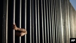 FILE - In this June 13, 2013, photo, hands from Daniel Zambrano of Tijuana, Mexico, holds on to the bars that make up the border wall separating the U.S. and Mexico as the border meets the Pacific Ocean in San Diego.