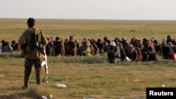 A fighter from Syrian Democratic Forces (SDF) stands near civilians, near the village of Baghouz, Deir Al Zor province, Syria, Feb, 22, 2019. 