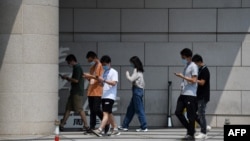 北京一群青年边走路边看手机。（2020年7月6日）