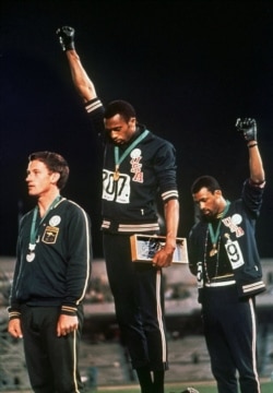 FILE - U.S. athletes Tommie Smith, center, and John Carlos stare downward and extend gloved hands skyward in a Black power salute after winning medals in the 200-meter run at the Summer Olympic Games in Mexico City, Oct. 16, 1968.