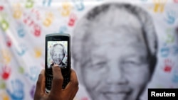 A well-wisher takes a picture of a banner with the image of former South African President Nelson Mandela, outside the hospital where he is being treated, in Pretoria July 18, 2013.