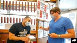 A Katz's Deli employee, left, checks the proof of vaccination from a customer who will be eating inside the restaurant, in New York, Aug. 17, 2021.