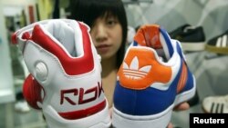 FILE - A saleswoman holds up athletic shoes by Reebok and Adidas in Taipei, Aug. 4, 2005.