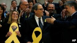 Newly appointed Catalan president Quim Torra, center, holds a yellow ribbon in support of Catalonian politicians who have been jailed on charges of sedition, at the end of a parliamentary vote session in Barcelona, Spain, May 14, 2018. 