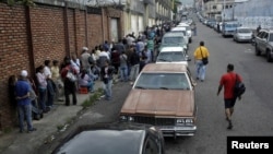 FILE - People line up outside a supermarket next to motorists queuing for gas near a gas station of the Venezuelan state-owned oil company PDVSA in San Cristobal, Venezuela, Nov. 10, 2018. 