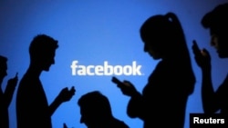 FILE - People are silhouetted as they pose with laptops in front of a screen projected with a Facebook logo, file photo. 
