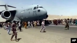 FILE - Hundreds of people run alongside a U.S. Air Force C-17 transport plane as it moves down a runway of the international airport, in Kabul, Afghanistan, Aug.16. 2021.